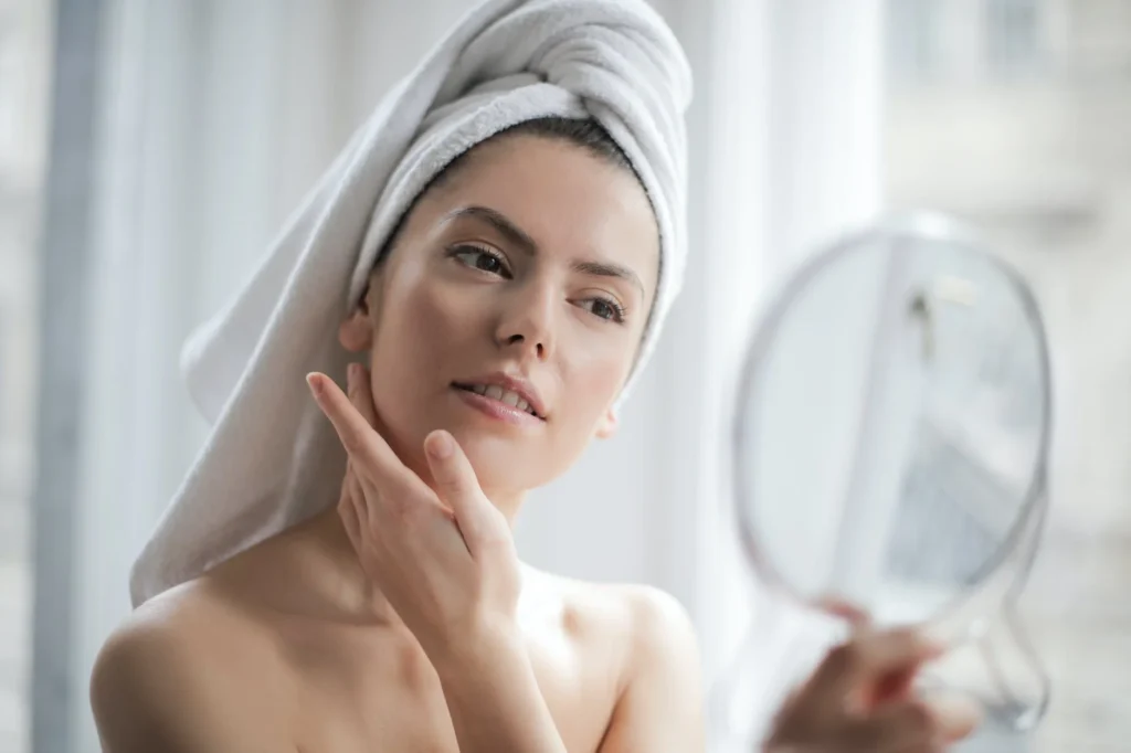 woman with white bath towel around her hair and looking in a hand held mirror, ultherapy vs hifu
